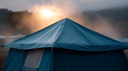 Misty sunrise illuminates a serene campsite with a prominent teal tent in the foreground evoking a sense of peaceful adventure