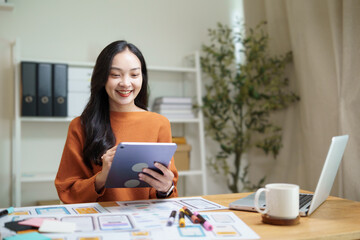 UX UI designer reviewing tablet app interface while surrounded by wireframe sketches at a modern workspace.