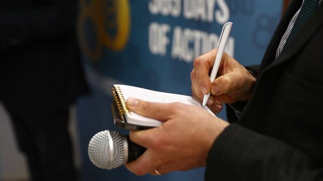 Businessman taking notes. Wide background . Journalist, reporter or correspondent in a suit taking notes on a notepad while holding a microphone during a media interview session. Journalism concept.