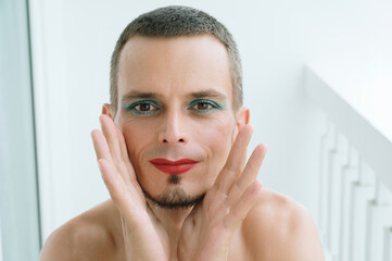 portrait of happy feminine gay man with makeup and cosmetics on face. Transgender male with red lipstick on lips and mascara on eyes