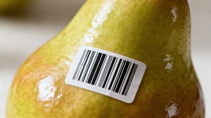 Yellowish green pear fruit displaying a printed black and white barcode sticker affixed tightly to its shiny, reflective skin.