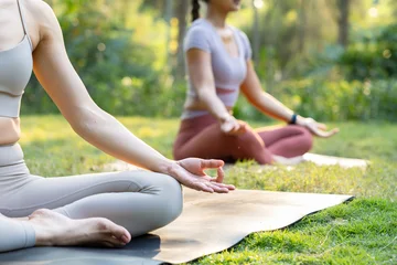 Fotobehang Lotusbloem Close-up of woman hand with lotus pose, doing yoga pose sitting on mat outdoors. Two Asian woman sitting in lotus pose meditating relaxing. Woman waring sportswear sit while meditating outdoors .  © SAT65