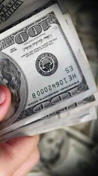 Hand holding stack of us one hundred dollar bills close up cash money background showing currency detail and selective focus concept for savings income payday business finance and wealth