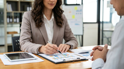 Businesswoman pointing at financial charts, discussing data analysis with a male client in a professional office meeting. Ideal for consulting, finance, and strategy