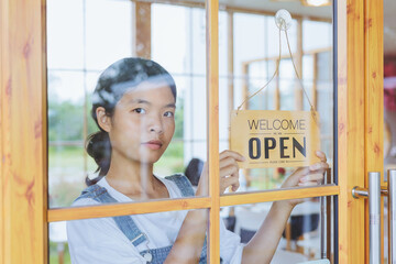 woman holding sign that says welcome to open in front of a window. The woman is business owner or employee