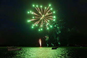 Green fireworks with a "chrysanthemum" pattern exploding over boats in the harbor during New Year celebrations
