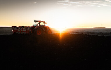 Fototapeta premium Tractor plowing field the land at sunset