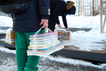 Volunteers carrying bundles of paper and books outdoors in snowy weather, illustrating community recycling efforts, paper collection, and environmental volunteer work.