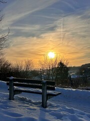 Snow-covered park bench at winter sunrise creates a peaceful urban landscape symbolizing calm mornings, cold weather, and quiet city life