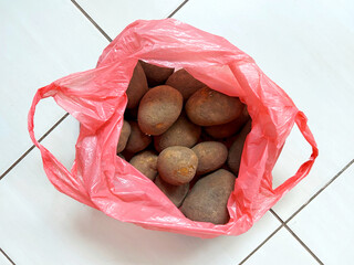 Fresh unwashed potatoes stored in a pink plastic bag on a kitchen floor, representing everyday food storage and household groceries