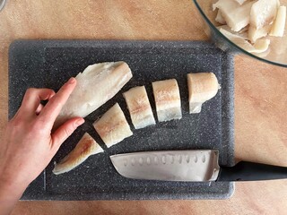 Hand slicing raw fish fillet on a cutting board with kitchen knife during home cooking preparation