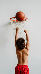 Back view of boy throwing basketball into hoop against white wall
