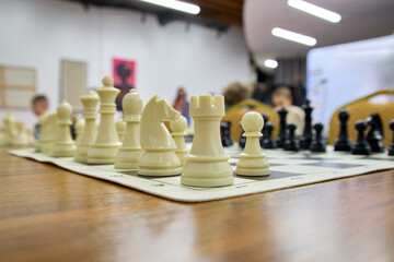 Chessboard with pieces in starting position on a wooden table in a social or competitive setting, capturing focus, strategy, and anticipation before a chess match.