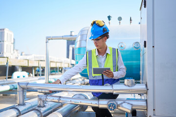 Technician working on tablet and checking pipeline valves or water tank area at urban industrial site