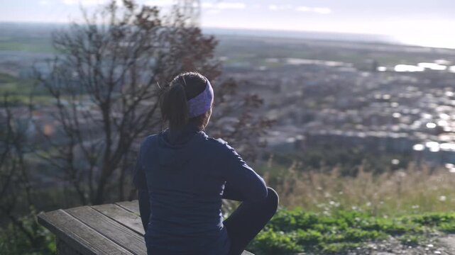 A woman meditates on a mountaintop as sunlight illuminates her.