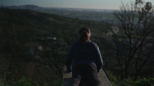 A woman does yoga on a bench at the top of a mountain.