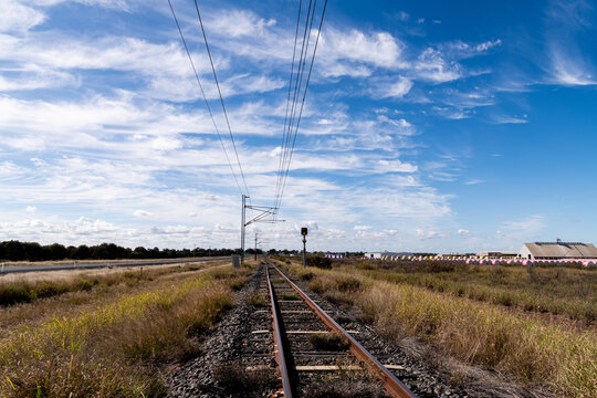 view along railway tracks lined with cotton bales and cloud patterns in blue sky