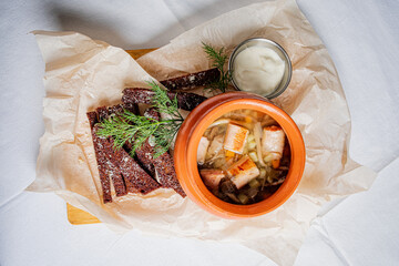 A rich, steaming bowl of soup rests on parchment, accompanied by dark bread and fresh herbs