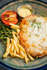 Crispy chicken fillet topped with cheese on a colorful plate with fries and grilled tomato