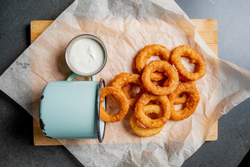 Platter of golden onion rings arranged with a side of tangy dipping sauce, inviting and delicious