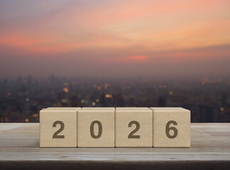 2026 letter on wood block cubes on wooden table over blur of cityscape on warm light sundown, Happy...