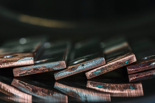 Close-up of oxidized and coated copper busbars in a dark industrial setting, showing surface texture and edges. Non-ferrous metal products prepared for recycling and metal processing.