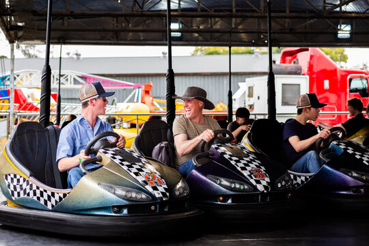 Middle aged man riding on dodgem cars show ride at event with teen son having fun together