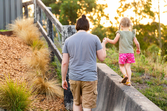 Little three year old child holding fathers hand while balancing on concrete fence barricade
