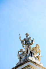 Obraz premium Marble statue of heroic male figures on top of the Vittoriano monument in Rome, Italy. The sculpture stands out against a clear blue sky. Historical landmark concept.