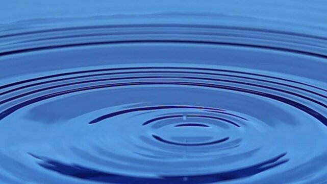 Close-up of a single water drop falling into clear water, creating smooth ripples and a delicate splash. Clean, minimal visual ideal for nature, purity, and liquid concepts.