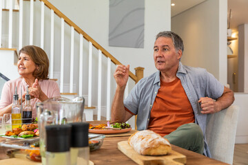 Senior couple talking while sitting in dining room at table with bread loaf, salad bowl