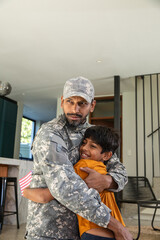 Indian father and son in camouflage uniform hugging inside home entry with small us flag © wavebreak3