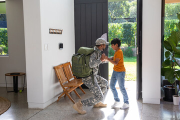 Middle eastern soldier father kneeling, greeting south asian son at home foyer with backpack
