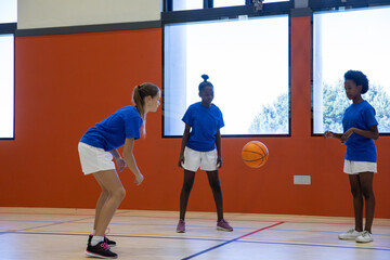 Diverse female basketball players practicing passing drill in school gym with basketball