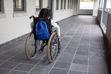 African american girl moving down tiled school corridor past railing with wheelchair, backpack