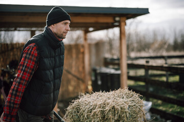 Man carries hay near barn during late afternoon