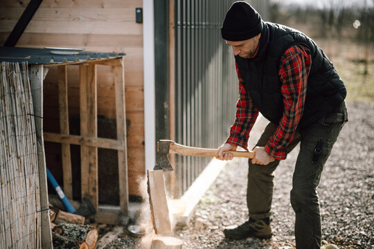 Man chops wood with axe near shed in the yard on a clear day