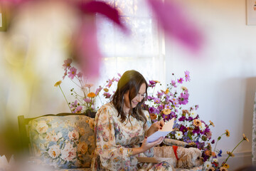 Woman on floral couch framed by flowers reads a card