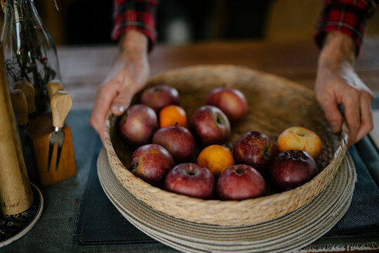 Person placing a basket of apples on a wooden table