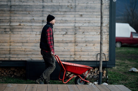 Worker moves a red wheelbarrow in front of a wooden wall