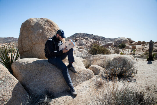 Man sitting on rock reading map in rugged desert landscape