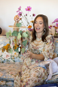 Woman on floral holds up a nursery mobile