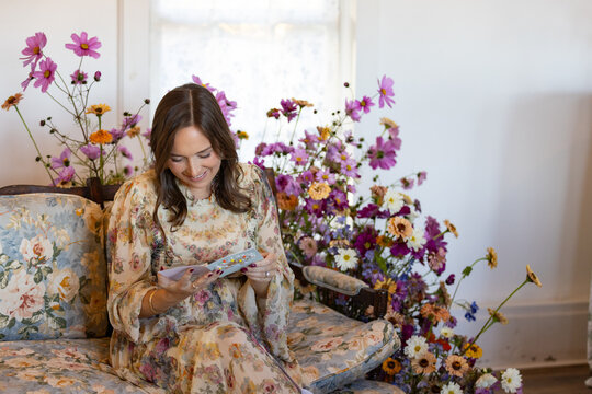 Woman on floral couch surrounded by flowers reads a card