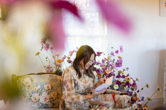 Woman on floral couch framed by flowers reads a card