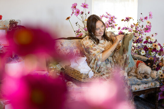 Woman on floral couch unpacks baby shower gifts surrounded by fl