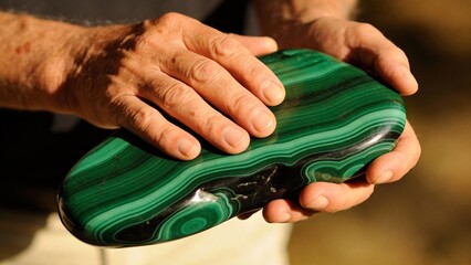 Hands holding polished malachite stone with green patterns outdoors  