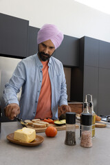 Indian man wearing turban chopping avocado, tomato slices on kitchen island cutting board © wavebreak3