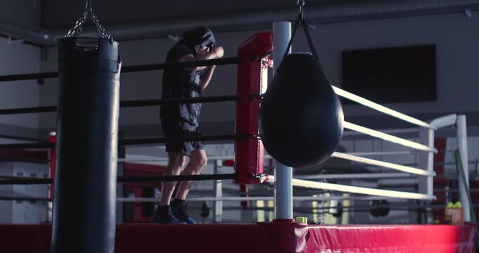 Male boxer is stretching his arms before training in a dark boxing gym. Dark gym scene shows a male boxer's silhouette stretching his arms before his workout. Slow motion zoom out 4K footage.