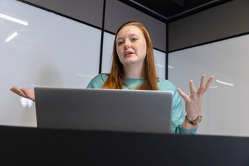 Mid adult woman presenting at conference table in conference room with laptop, wristwatch