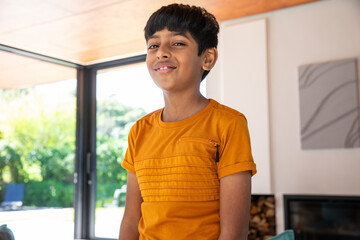 Naklejka premium Indian boy standing in living room in bright orange t-shirt with zip pocket under wood ceiling
